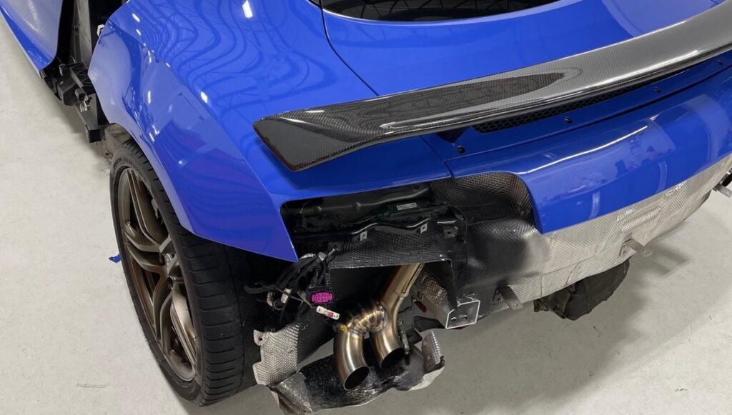 A blue car with a damaged rear end is sitting on a white surface.