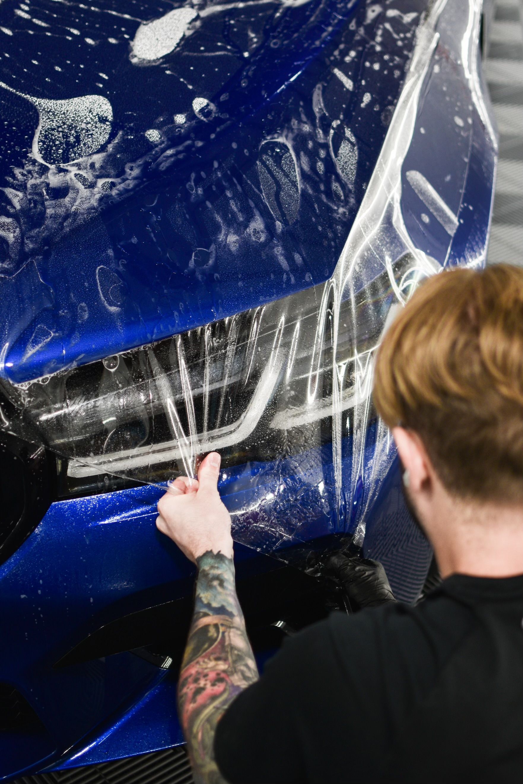 A man is applying a protective film to the headlights of a mercedes benz.