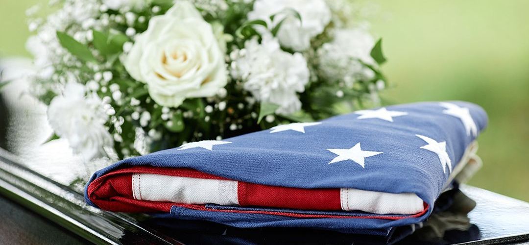 Folded American flag with white roses and greenery.