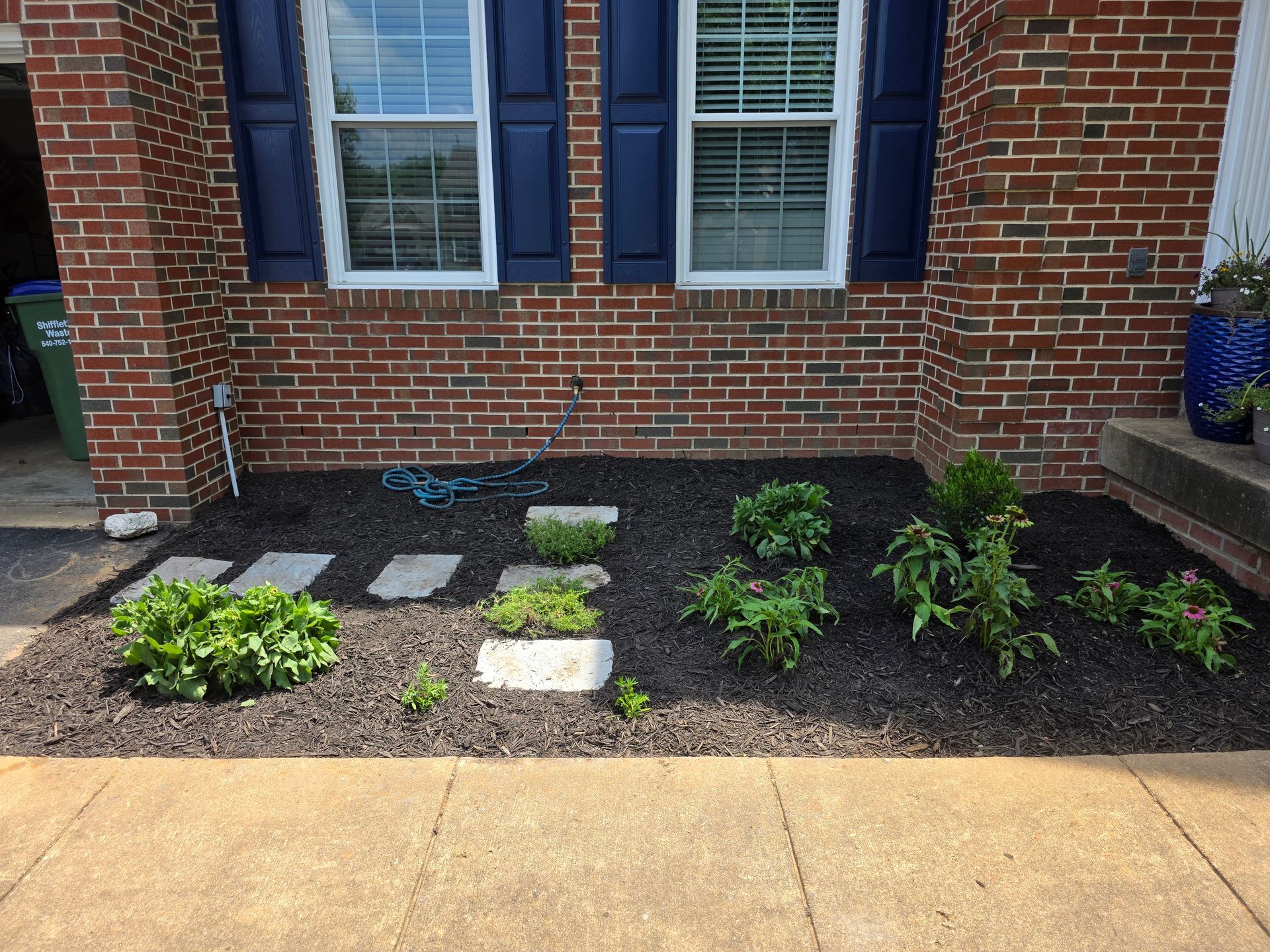 Freshly mulched garden bed by a brick house with small plants and a yard sign