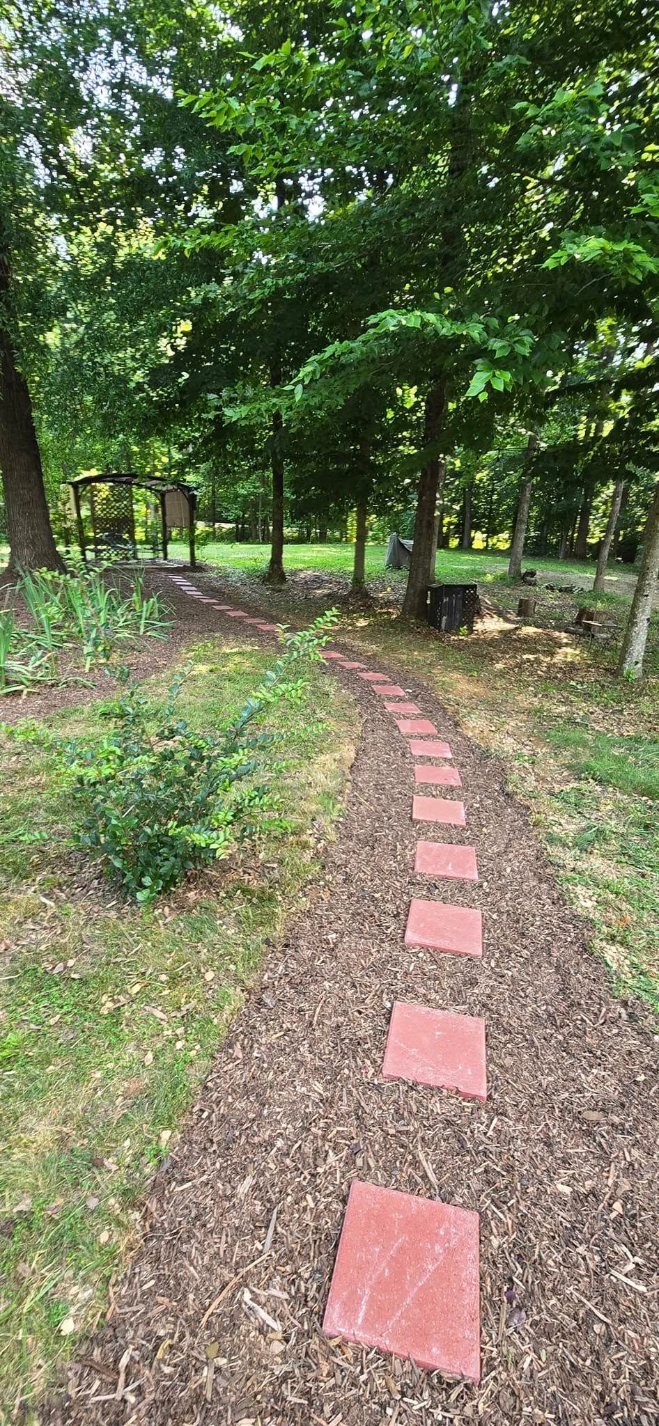 Narrow garden path with red stepping stones winding through green trees and shrubs