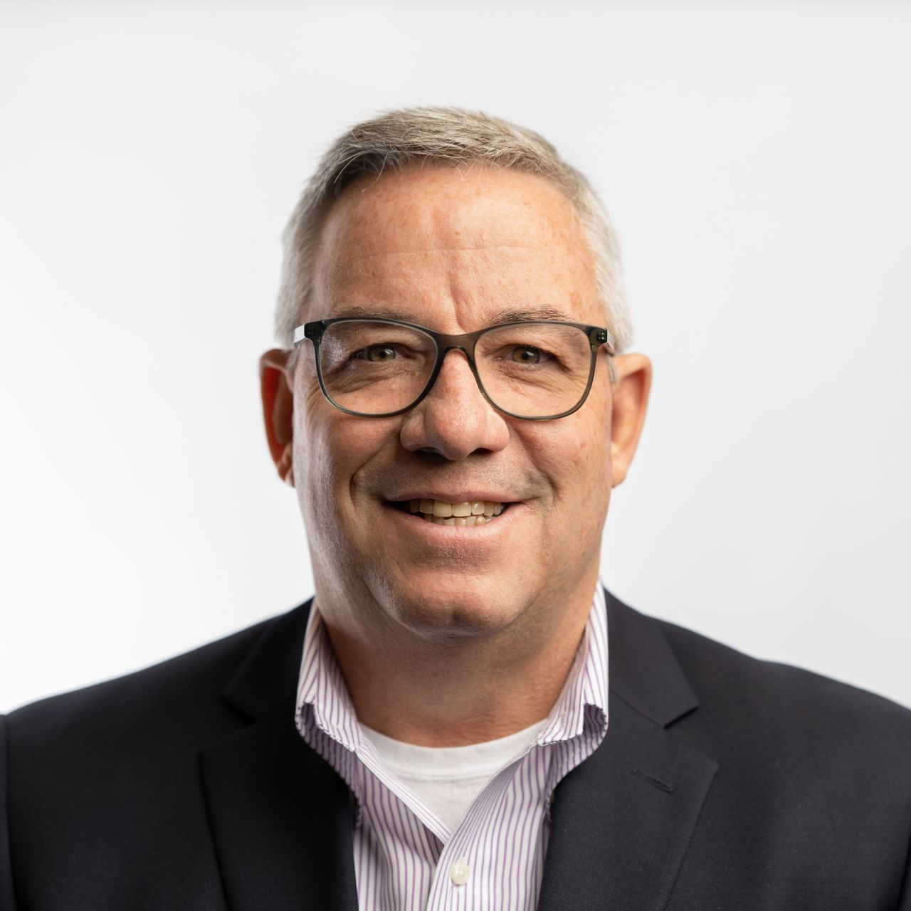 A man wearing glasses and a suit is smiling for the camera