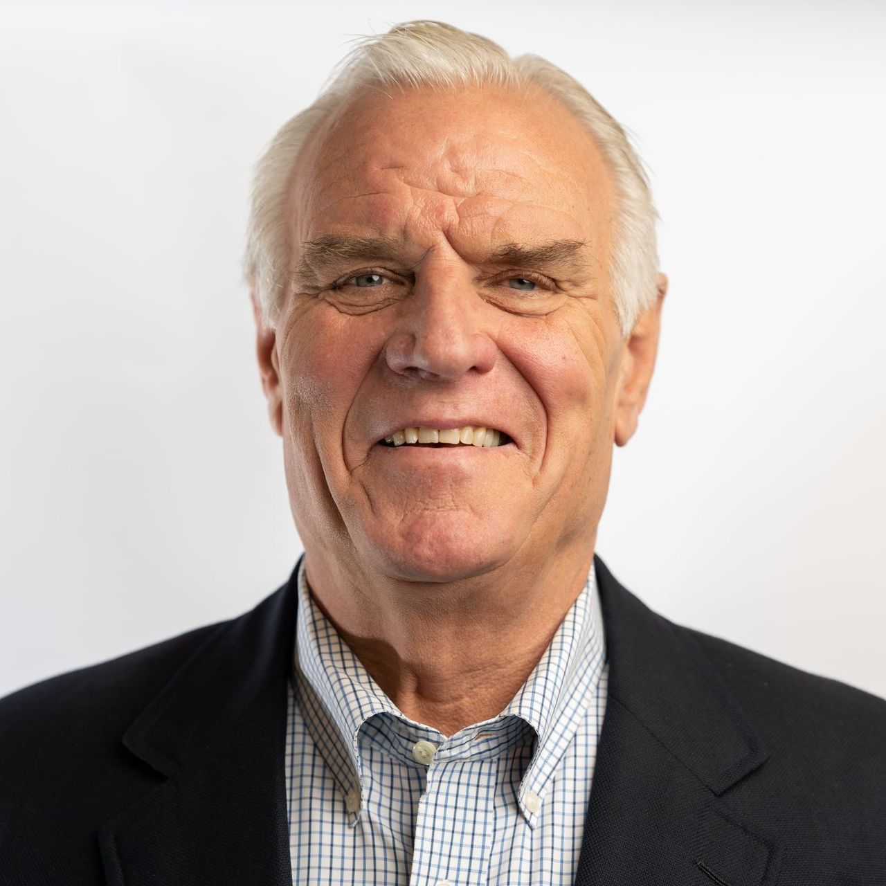 A man in a suit and plaid shirt is smiling for the camera.