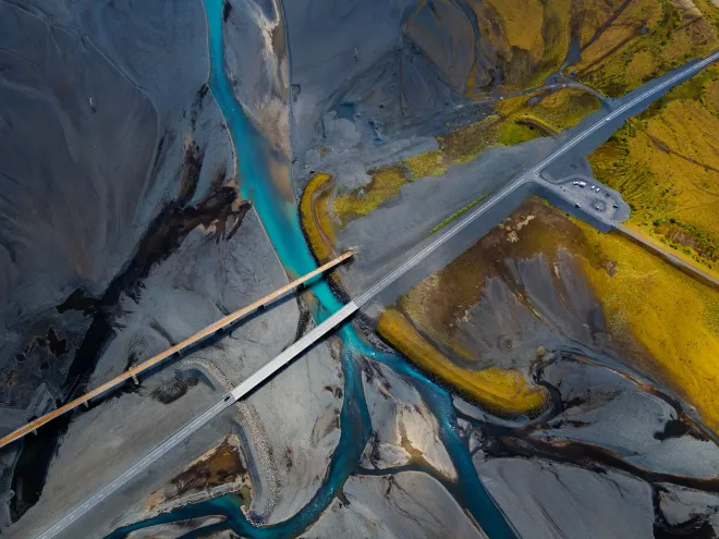 Aerial view of a bridge crossing a winding blue river through gray and yellow terrain