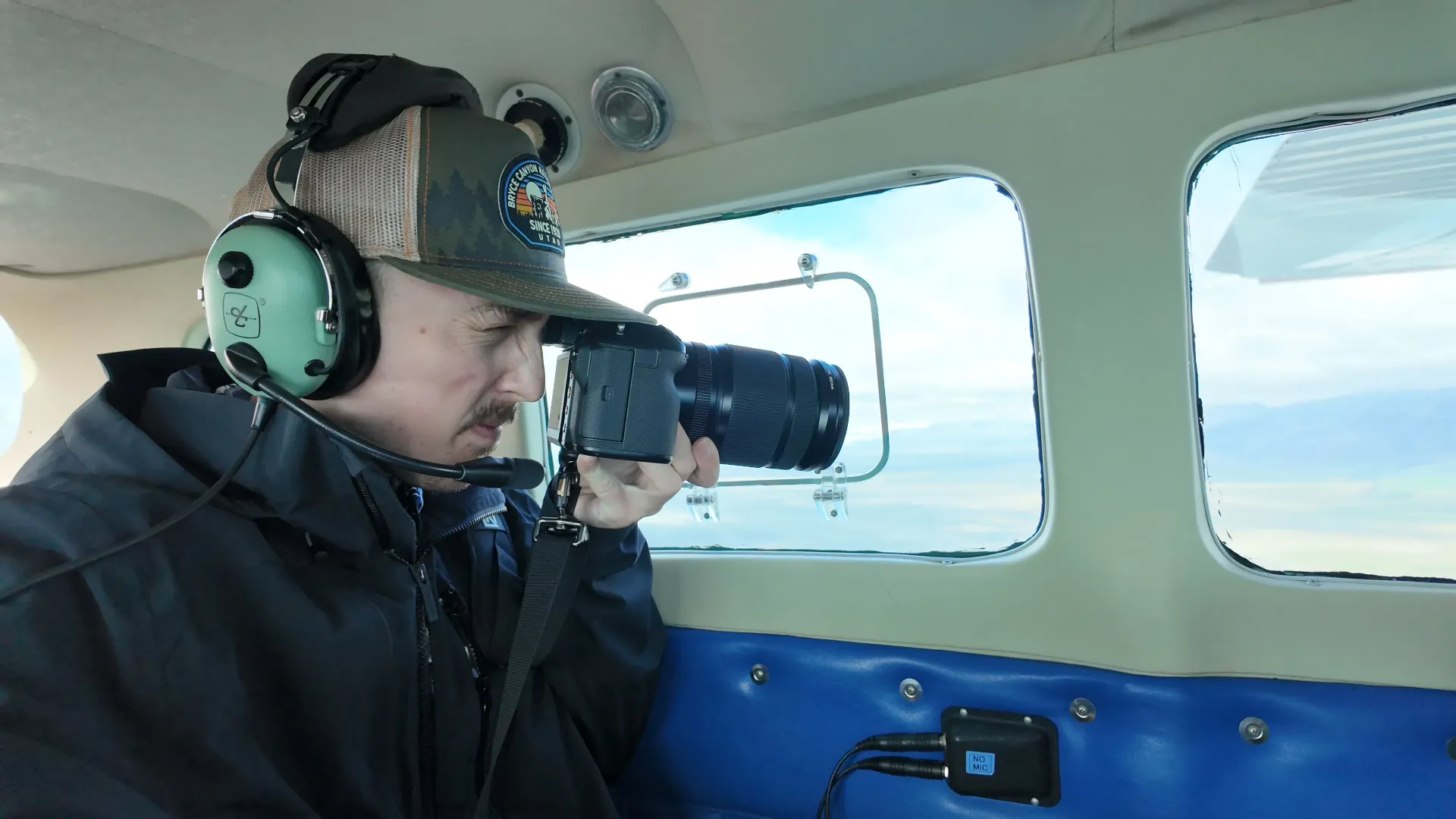 Person wearing a headset photographs through a small airplane window during flight