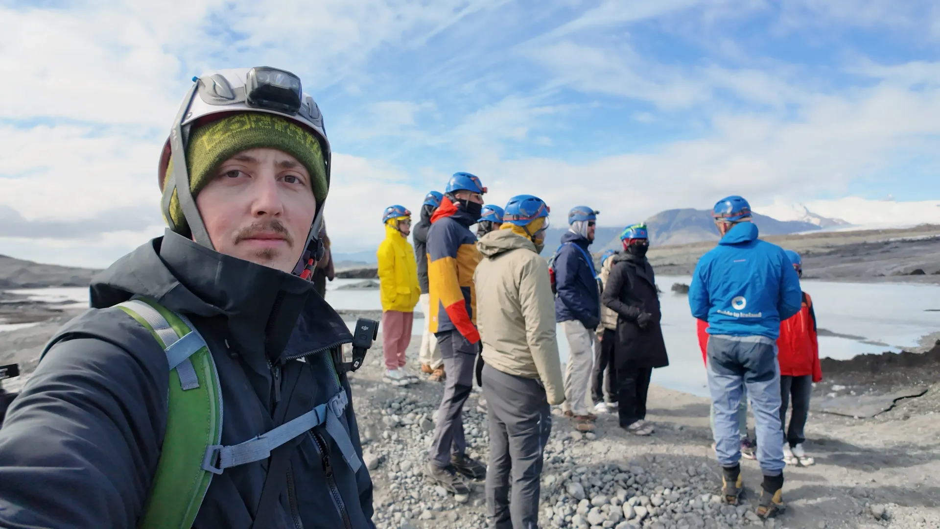 Snow-covered mountain overlook with a group in winter gear; one person takes a selfie in the foreground.
