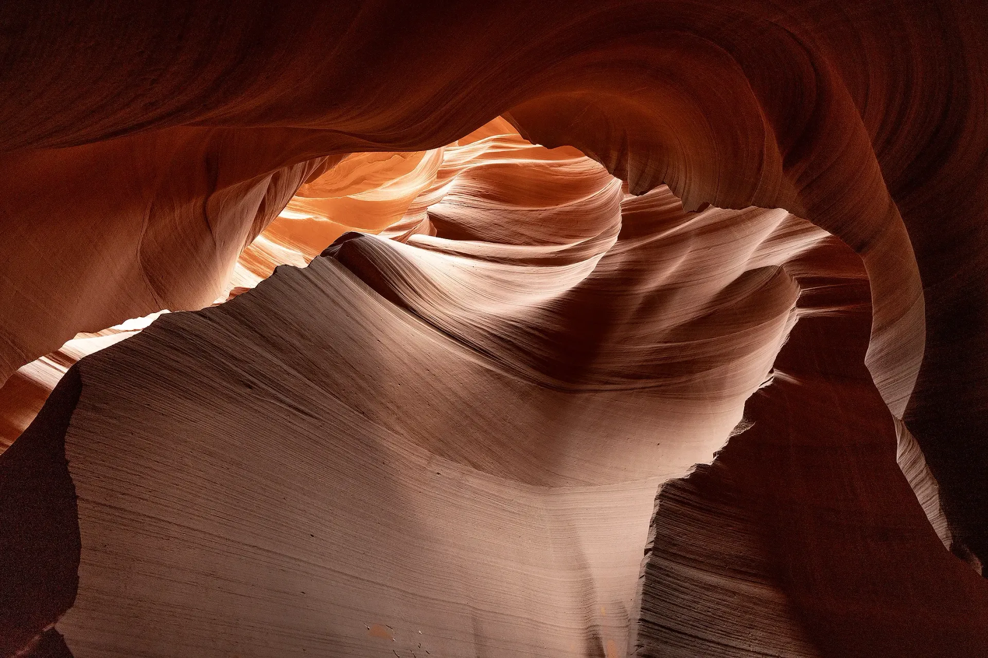 Sunlight beams into a narrow sandstone canyon with layered, swirling rock walls.