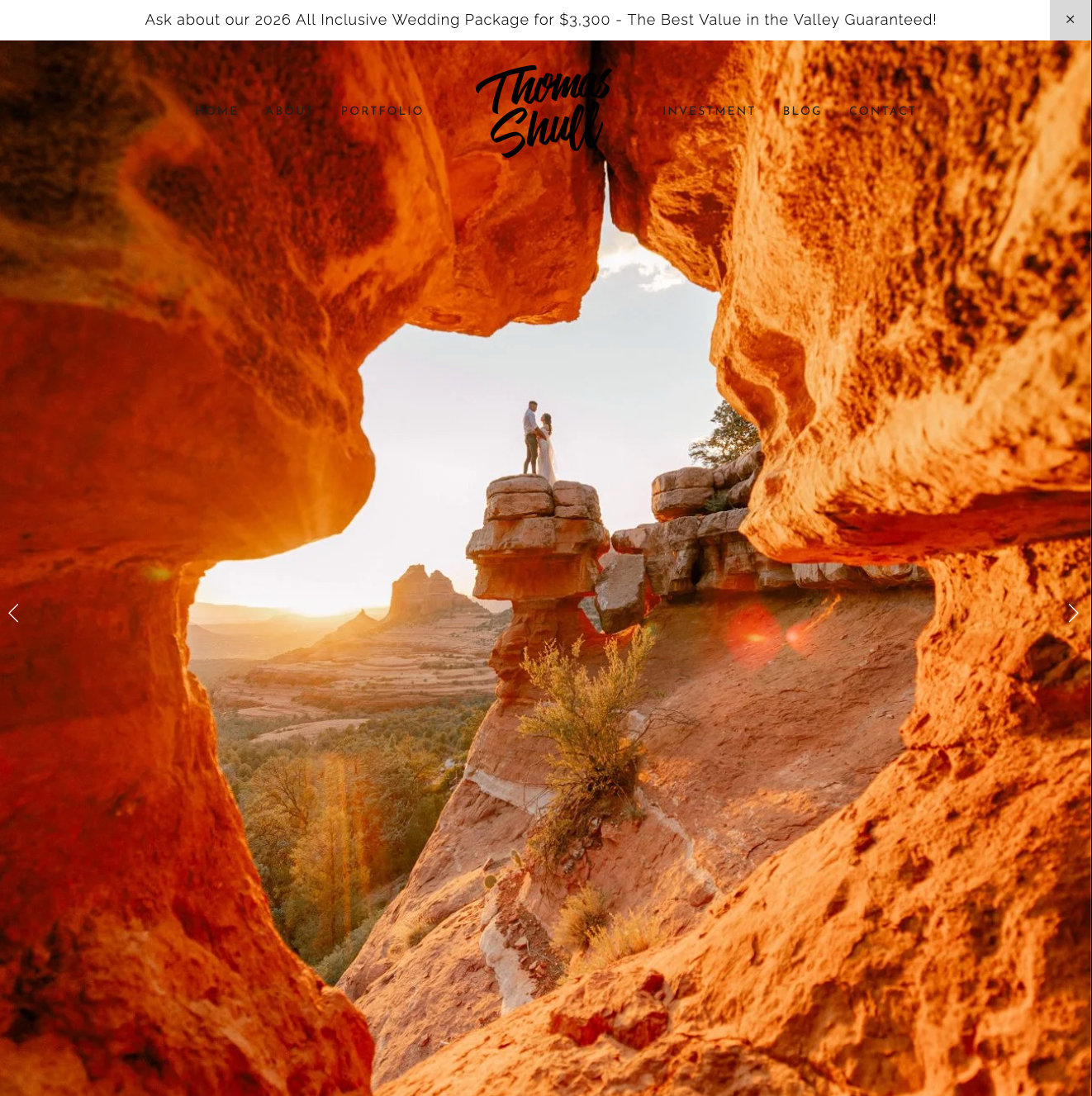 Sunlit canyon view through orange rock arch, with a person standing on a rocky outcrop at center.