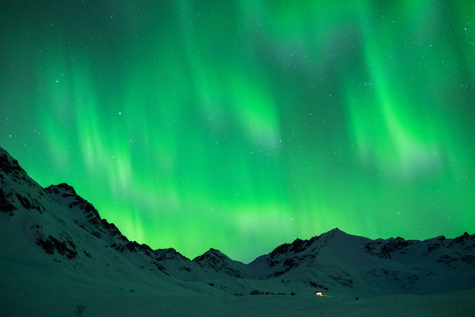 Green aurora lights over dark snowy mountains at night