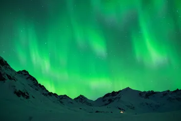Green aurora lights over dark snowy mountains at night