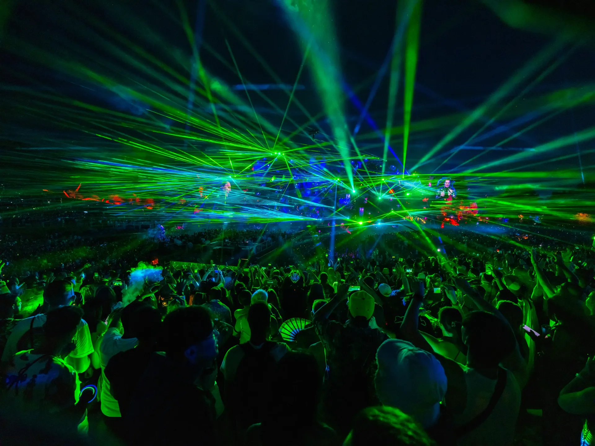 Crowd at a concert under vivid green and blue laser lights in a dark arena
