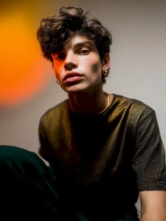 Portrait of a person with curly hair in a black shirt against a warm orange background
