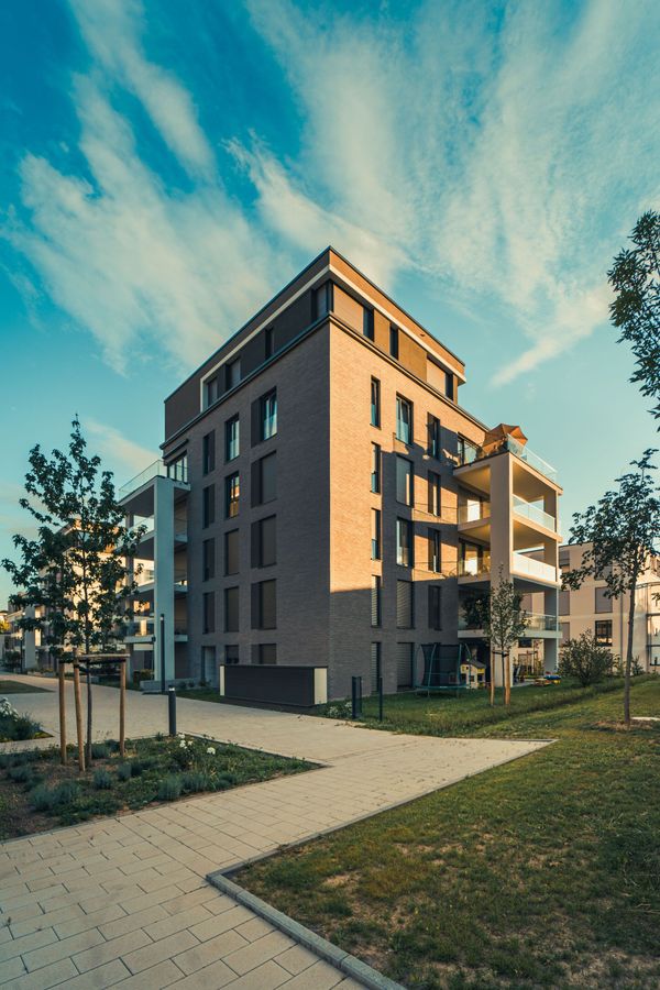 Modern apartment building at sunset with a paved path, trees, and blue sky.