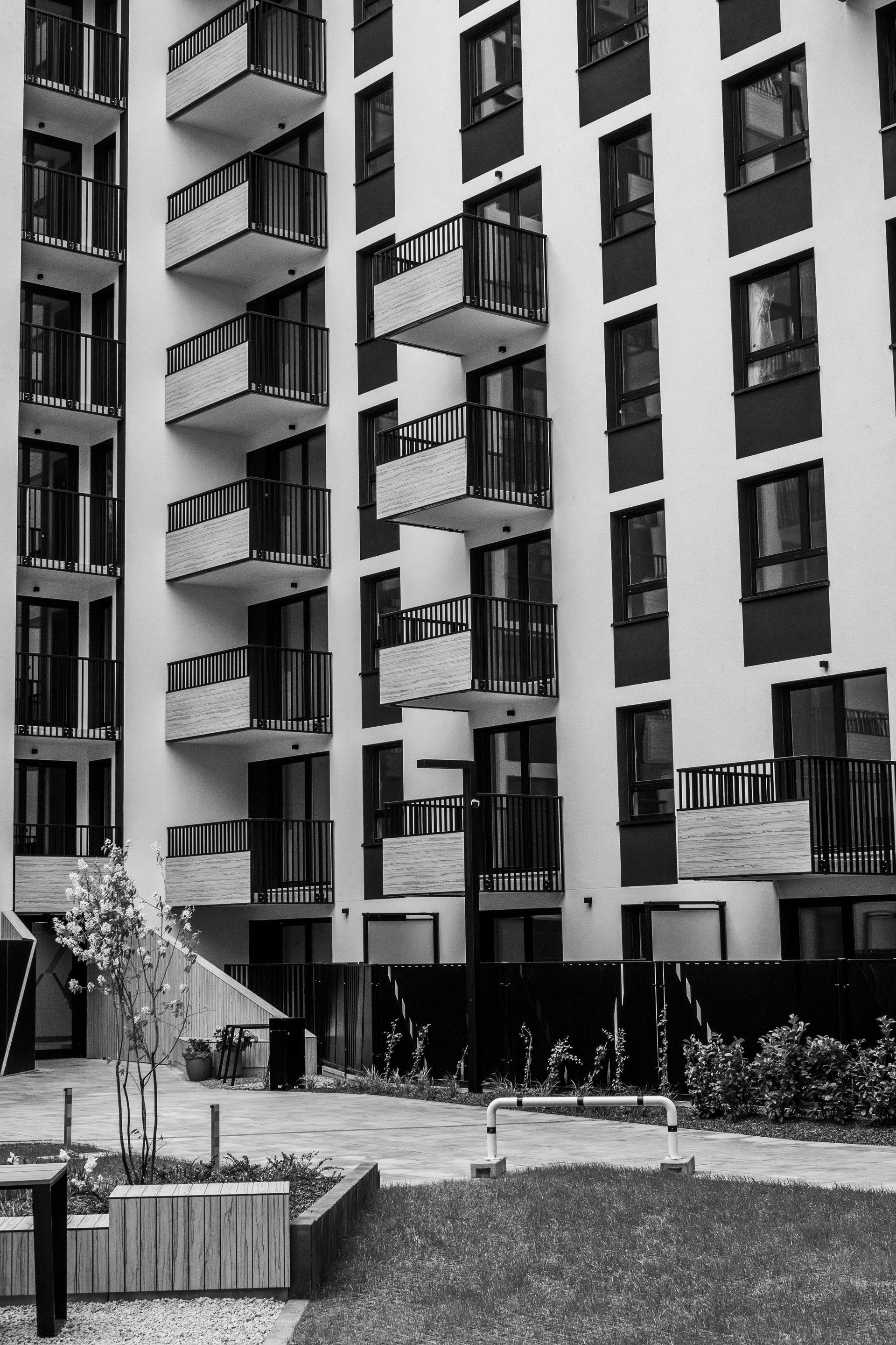 Black-and-white photo of apartment buildings with balconies, a courtyard, and landscaped plants.