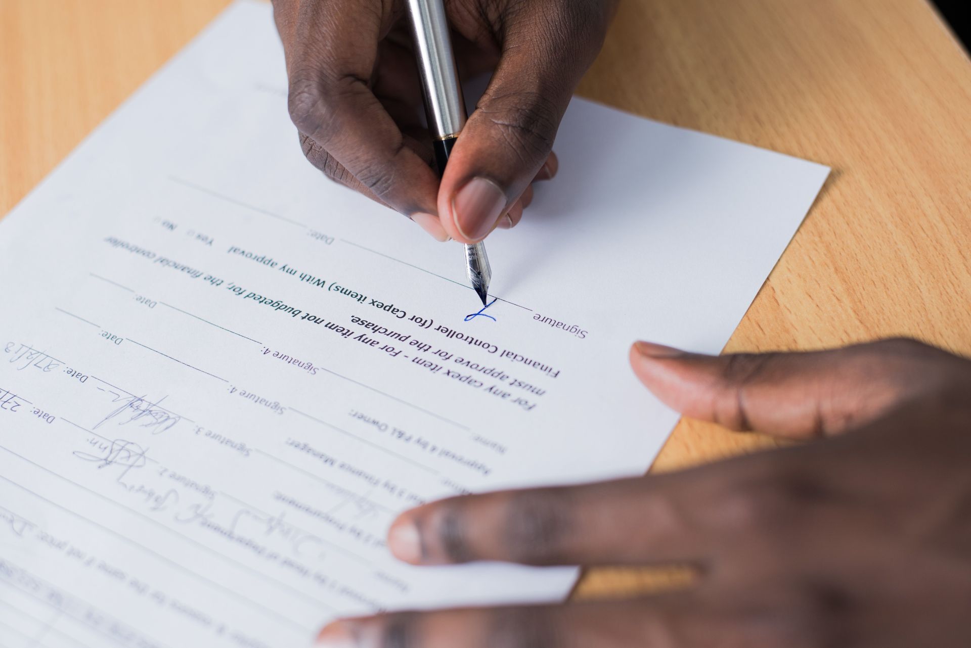 Hand writing on a white form with a pen at a wooden desk