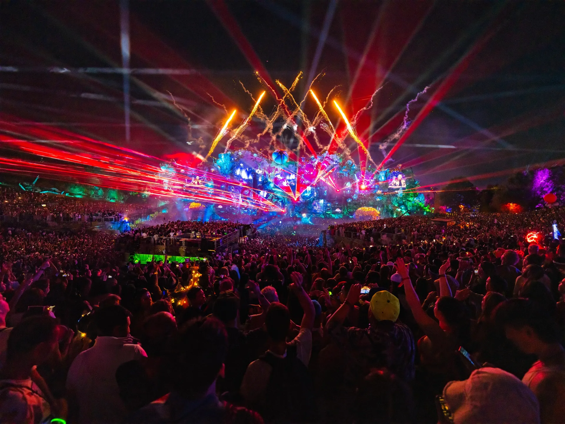 Crowd at a nighttime concert with colorful laser lights and fireworks over the stage