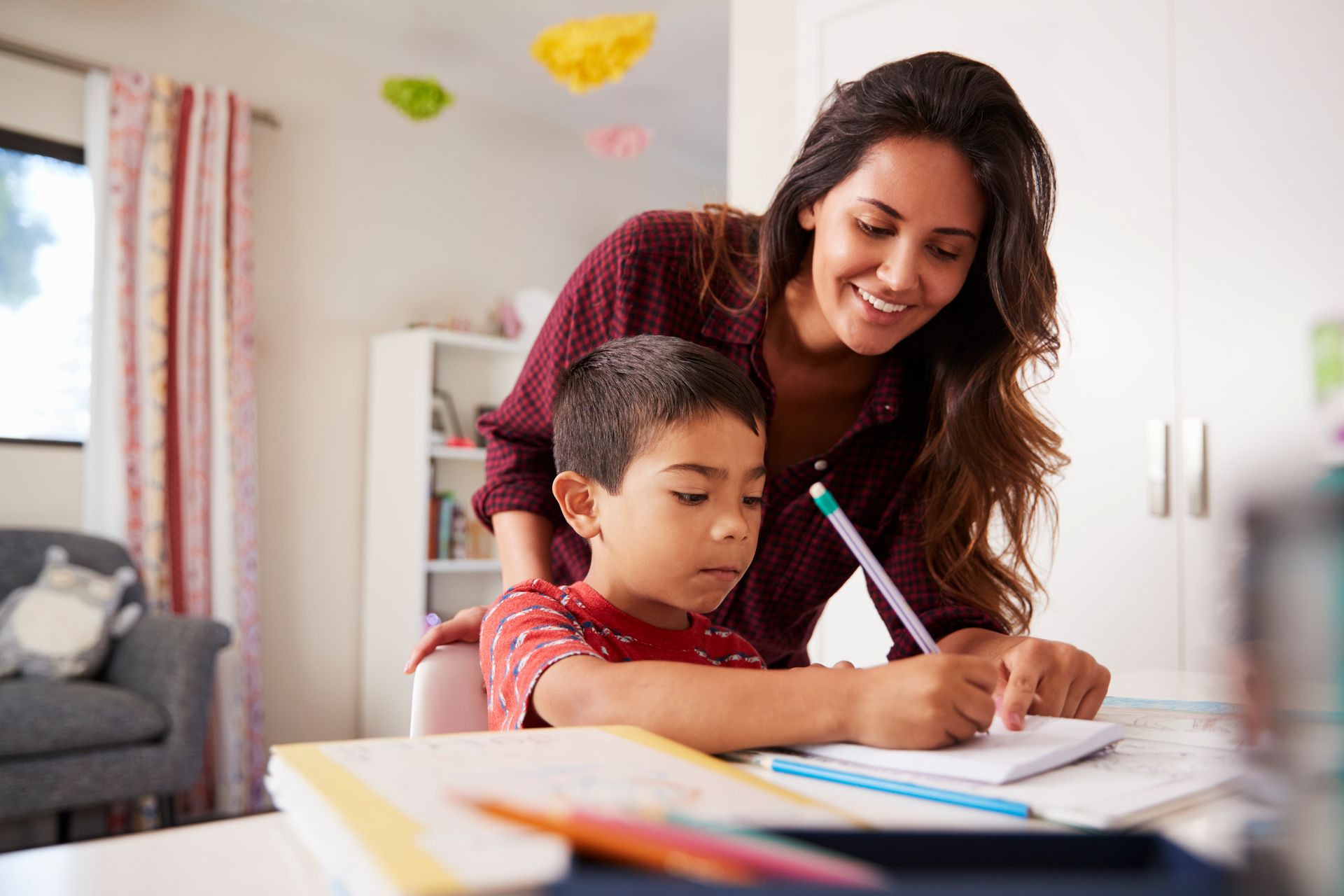 A woman is helping a young boy with his homework at a table.