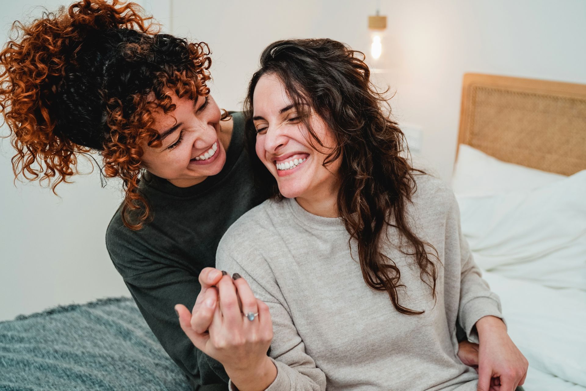 Two women are sitting on a bed laughing and hugging each other.