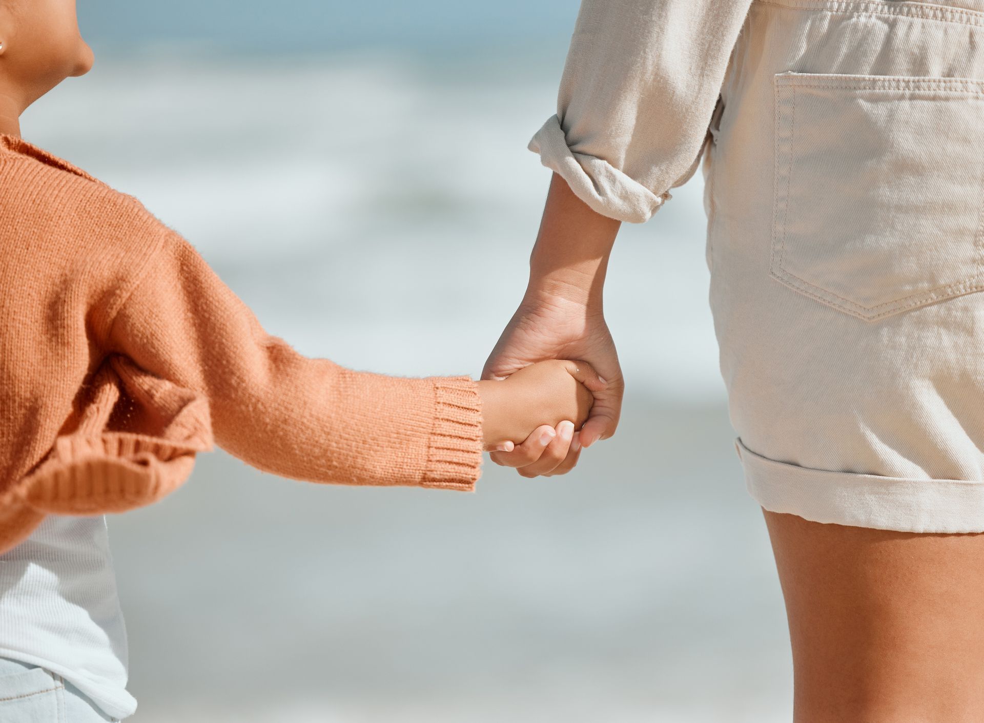 A woman and a child are holding hands on the beach.