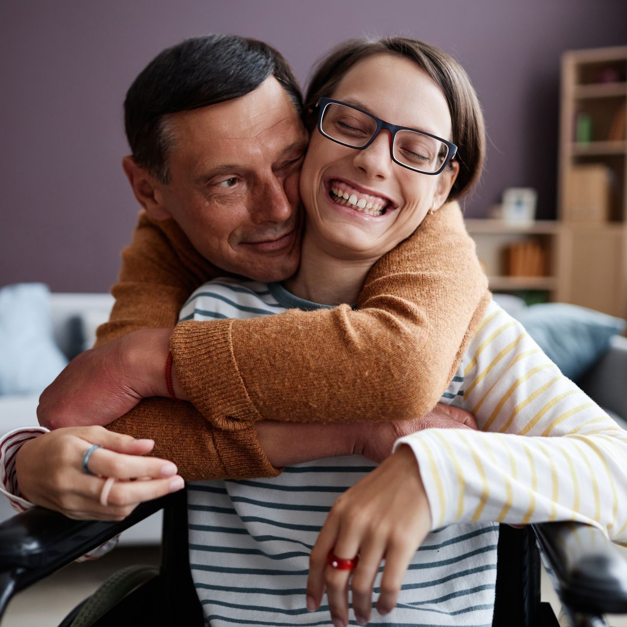 A man is hugging a woman in a wheelchair who is wearing glasses.