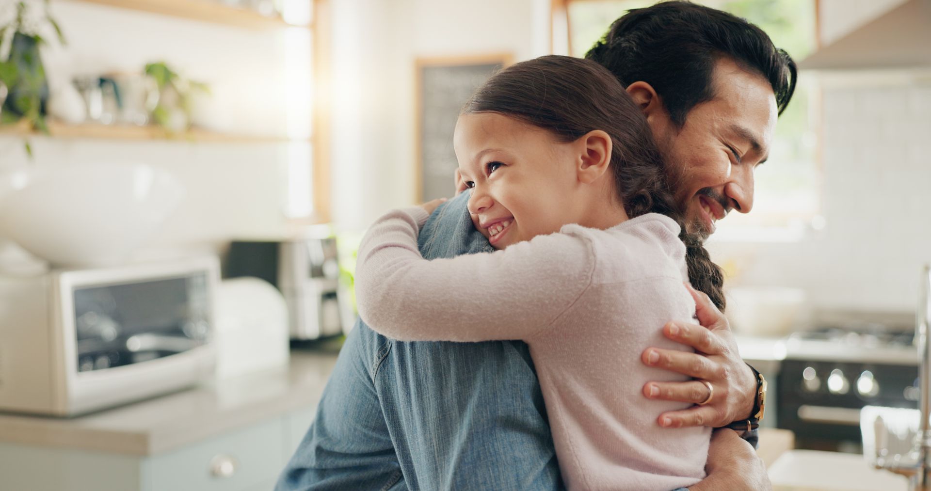 A man is hugging a little girl in a kitchen.