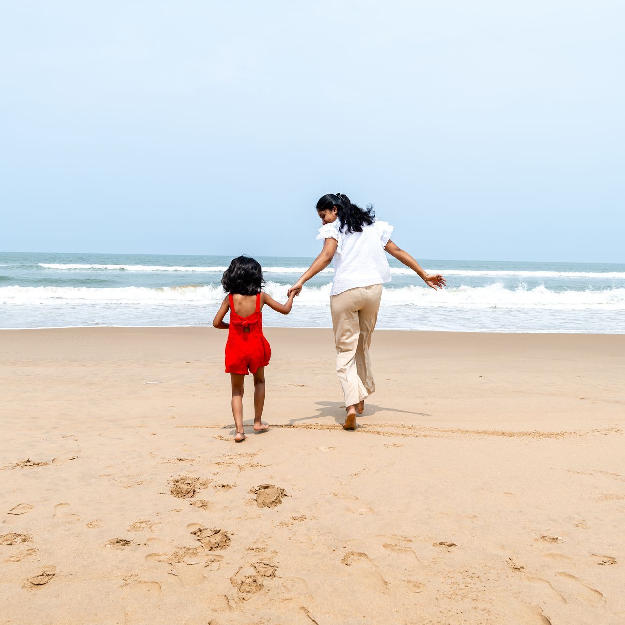 A woman and a little girl are walking on the beach holding hands