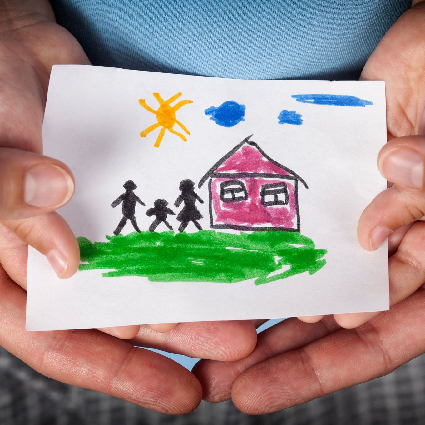A person is holding a drawing of a family and a house