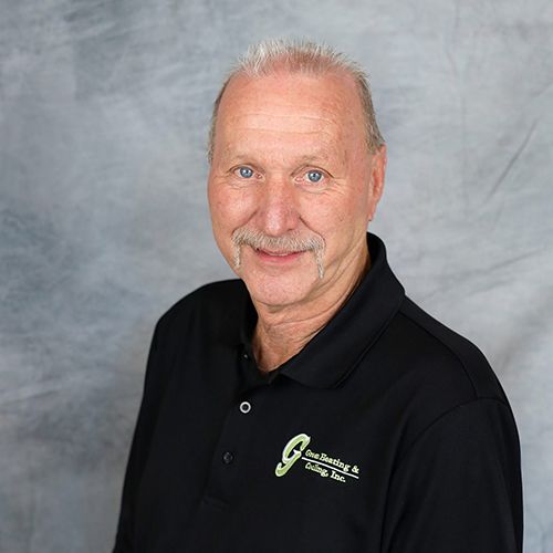 Man in black polo shirt smiles, posing against a mottled gray backdrop.