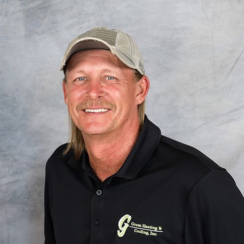 Man wearing a cap and black polo shirt with logo, smiling against a gray background.