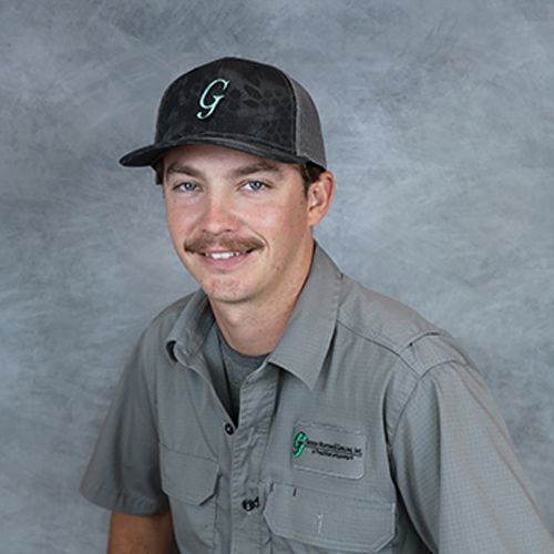 Man in gray shirt and cap, smiling, with a mustache. The cap has a