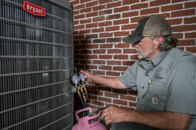 HVAC technician with gauges, examining a Bryant air conditioning unit near a brick wall.