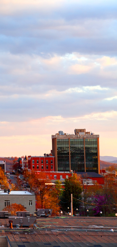 City skyline at sunset with a glass office tower, red brick buildings, and pastel clouds