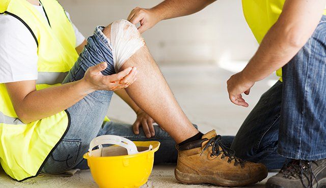 A construction worker is sitting on the floor with a bandage on his knee.
