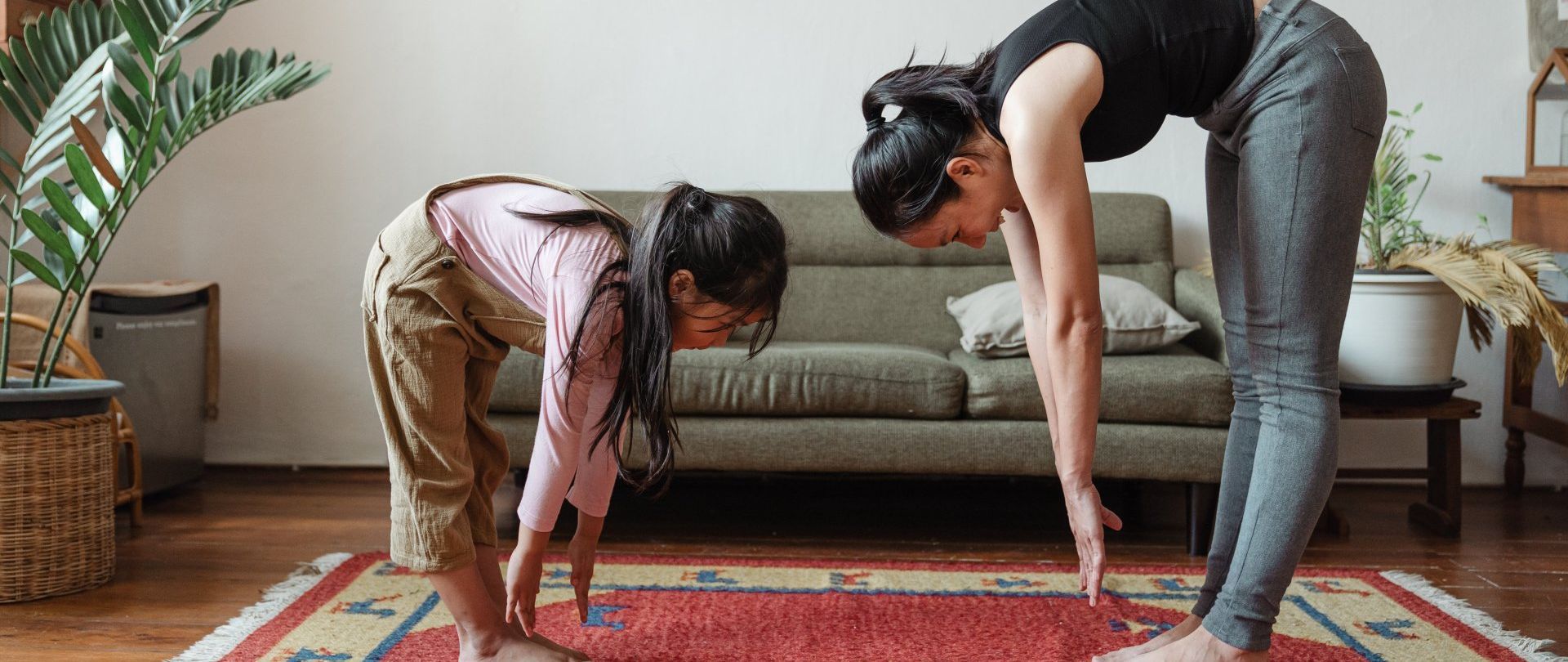 A woman and a little girl are doing yoga together in a living room.