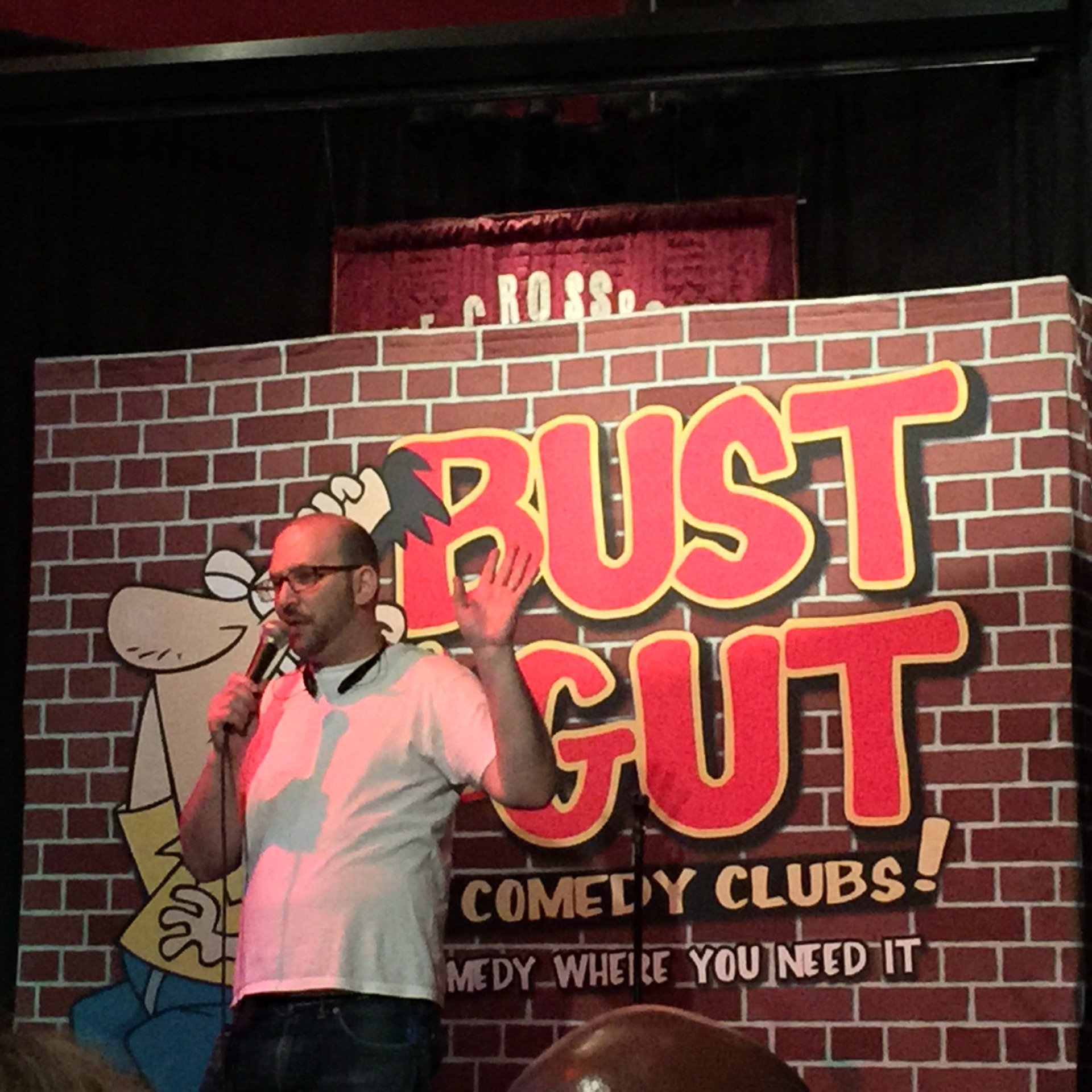 Man on stage, holding microphone, in front of a 