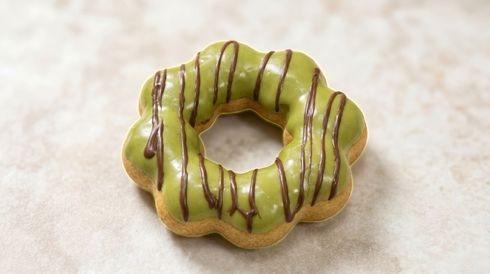 Green ring-shaped pastry with chocolate drizzle on a light surface