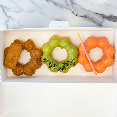 Box of assorted colorful glazed donuts arranged in a grid on a white surface