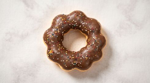 Chocolate-glazed donut with colorful sprinkles on a white surface