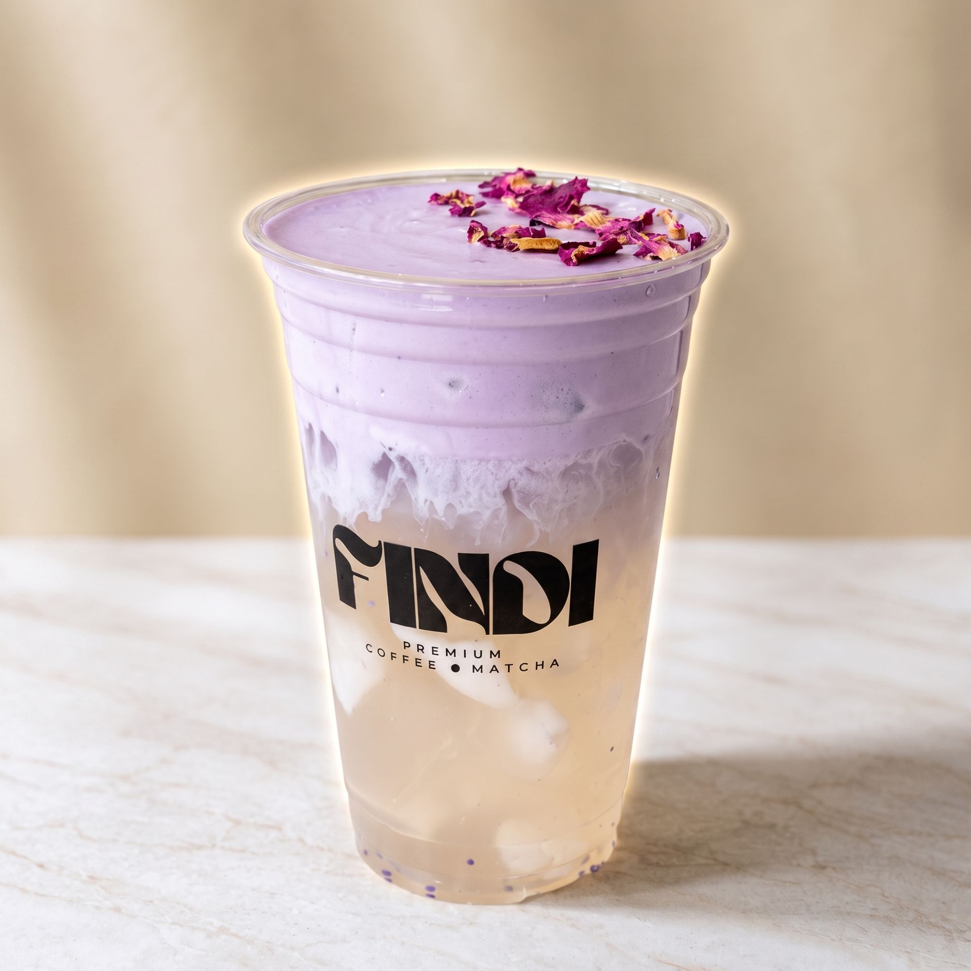 Lavender and peach layered iced drink in a clear cup with flower petals on top, on a marble surface