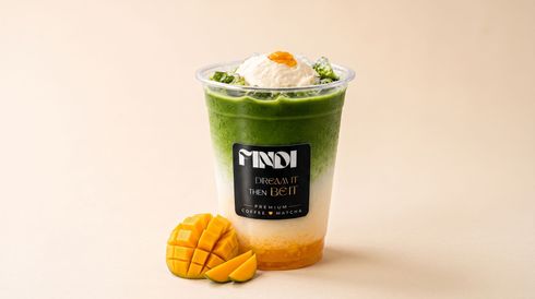 Iced green matcha drink in a clear cup with mango slices on a beige background