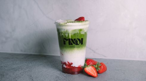 Strawberry green and white layered drink in a cup, garnished with cream and strawberries on a gray surface