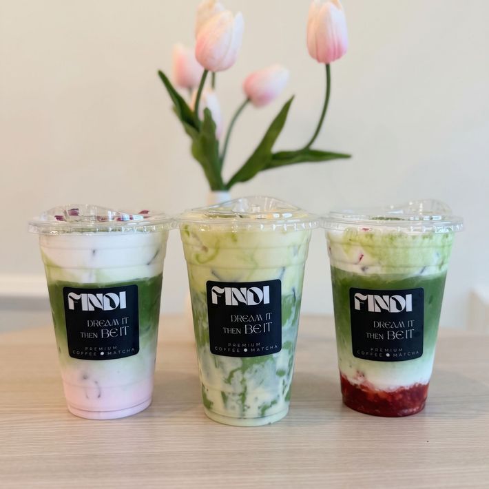 Three layered iced drinks in clear cups on a table, with pink tulips in the background.