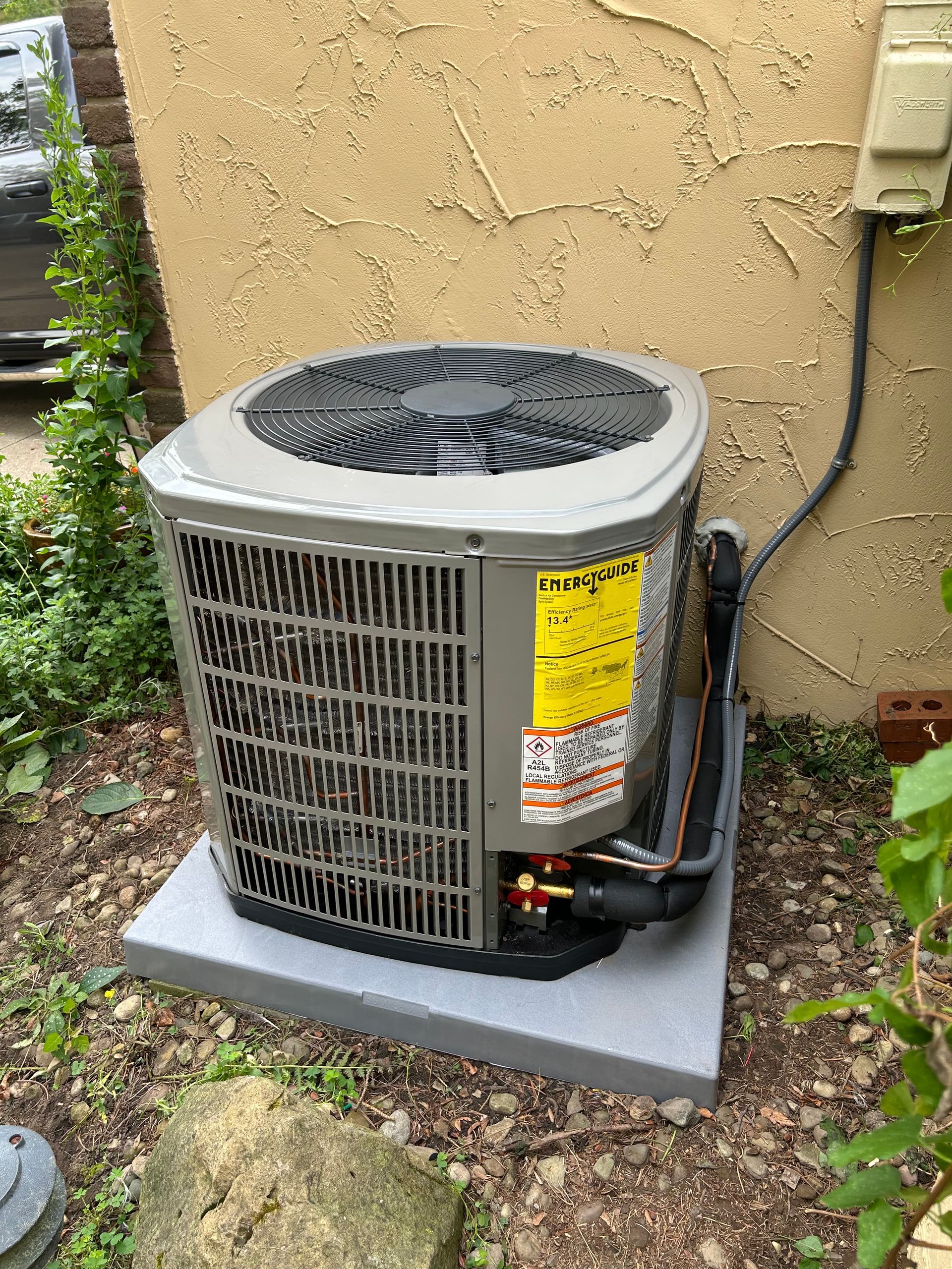 Air conditioning unit on a gray concrete pad next to a stucco wall.