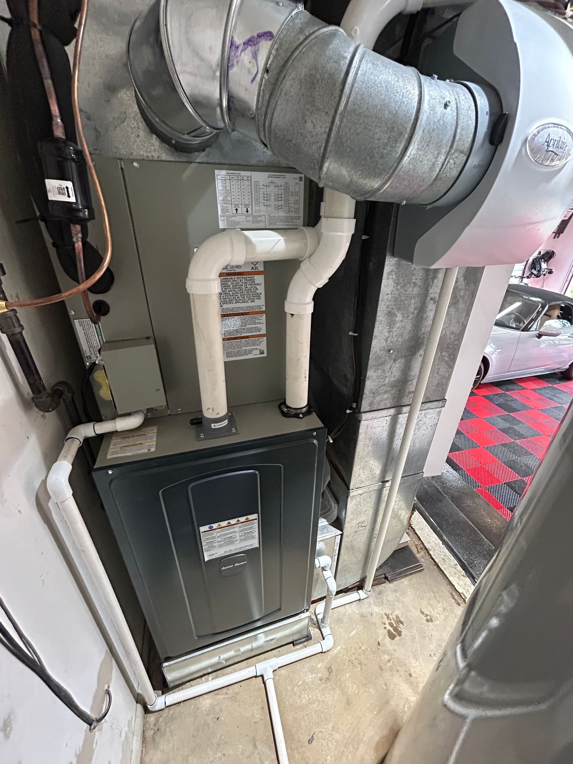 Furnace unit with ductwork in a basement setting. Gray and white with some exposed copper piping.