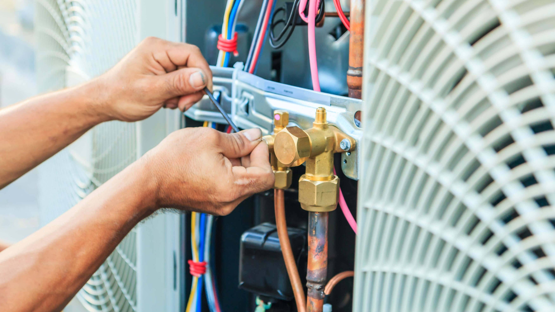 A technician repairing an air conditioning unit; hands working with copper pipes and wires.