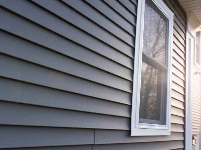 Gray house siding with a white-framed window and sunlight on the exterior wall
