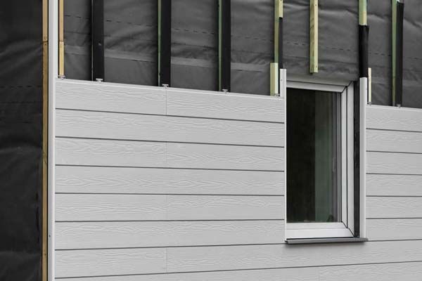 Gray siding being installed on a house exterior, with an open window and exposed framing above.