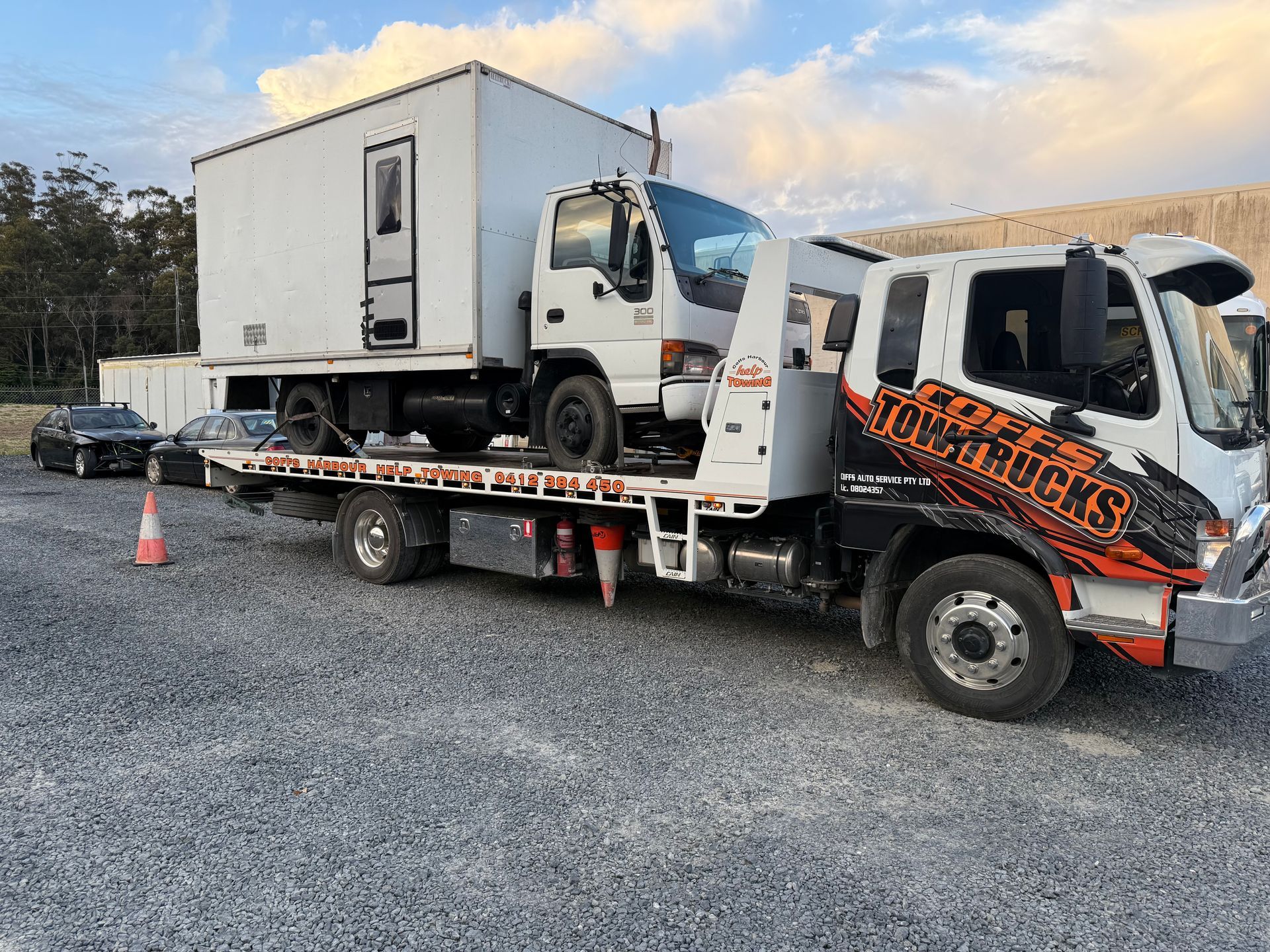 Tow Truck Carrying A White Box Truck On A Gravel Lot — Coffs Tow Trucks In Sawtell, NSW