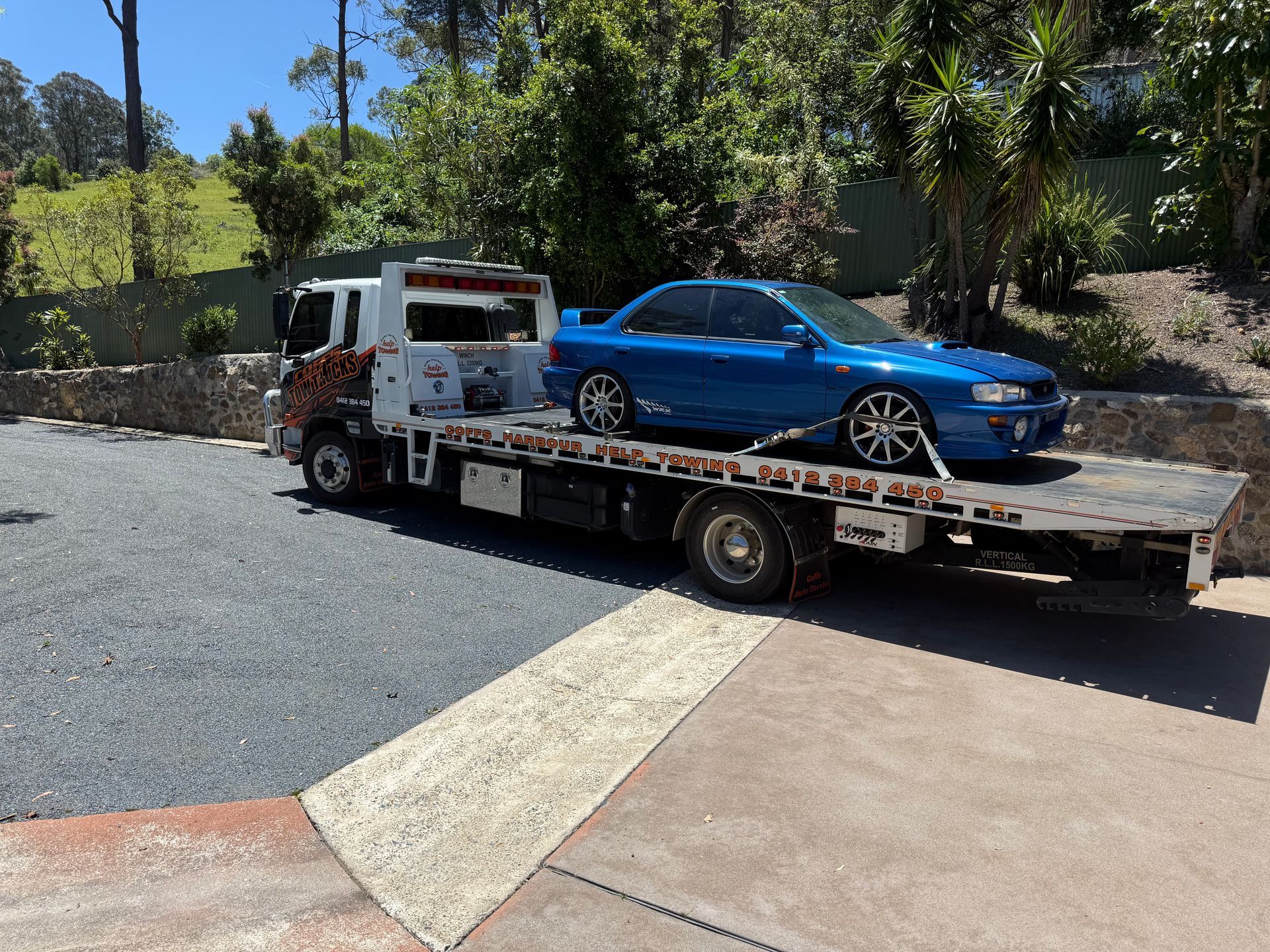Tow Truck Hauling A Blue Sedan On A Flatbed In A Sunny Driveway — Coffs Tow Trucks In North Boambee Valley, NSW