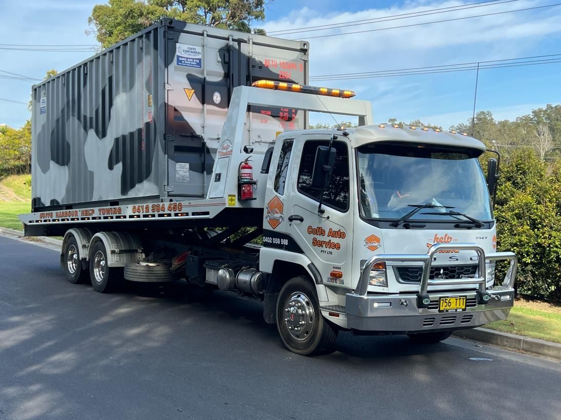 A Tow Truck is Carrying a Container Down a Road — Coffs Tow Trucks In North Boambee Valley, NSW